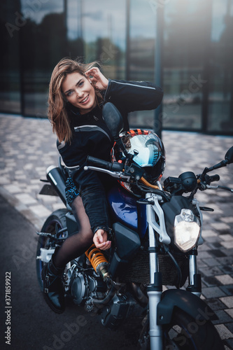 Young cute female driver and dark modern bike. Urban powerfyl vehicle. Motosport hobby.