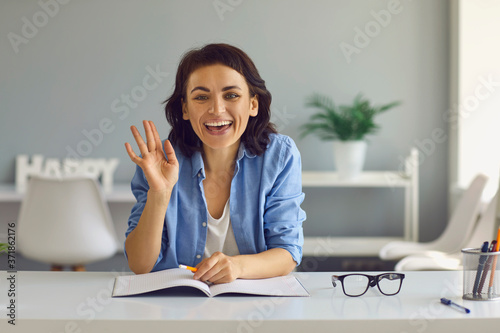 Young smiling woman looking at camera and greeting people online at home photo