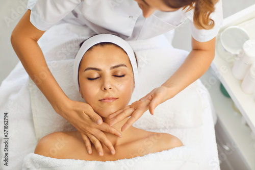 Beautician makes a facial massage to a woman in a spa salon. Woman receiving face protection treatment procedures