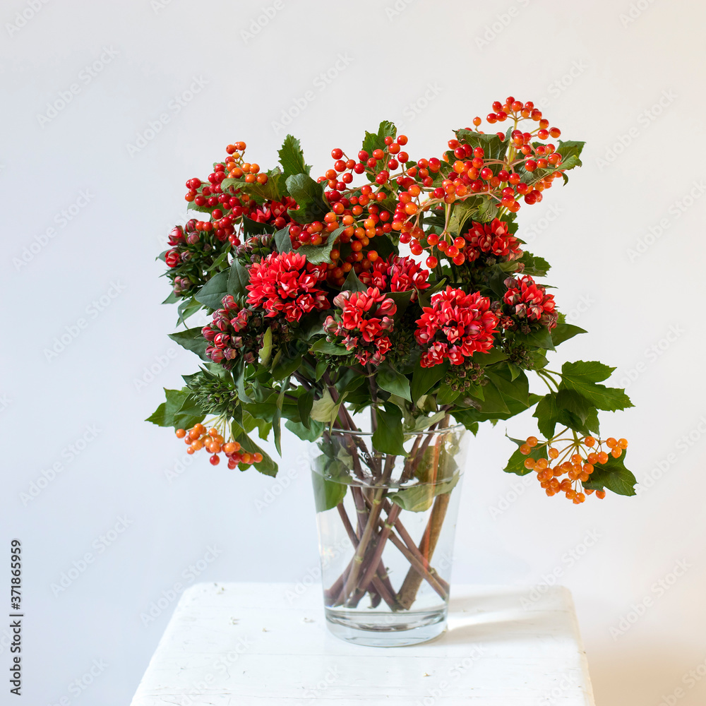 Hypericum and hawthorn flowers in a vase on a white stool on a white background. Hypericum and hawthorn flowers in a vase on a white stool on a white background.