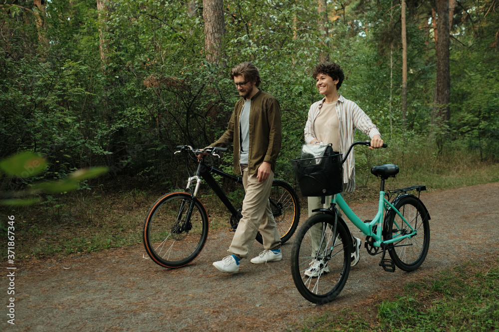 Young cheerful man and woman in casualwear moving down road after cycling