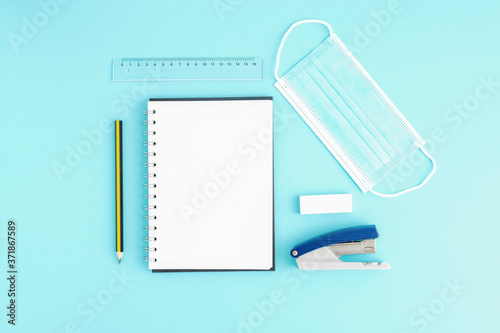 Blank open notebook with blank sheets and around stationery and medical protective mask, stapler, ruler, pencil. Space for text, office work during quarantine and virus photo