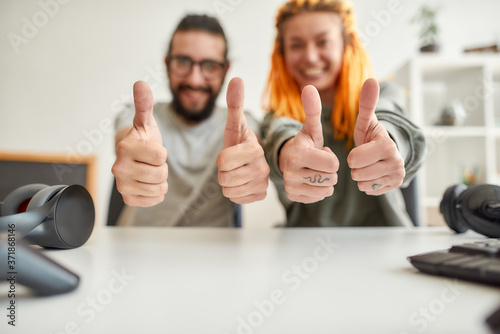 Cheerful man and woman showing thumbs up at camera. Young male and female technology blogger recording video blog or vlog about new gadgets at home