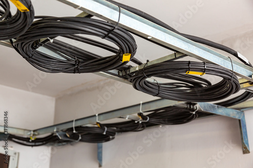 Cable management. Working wires, black cables wound into a coil, a circle. Rings of coiled wires, wire roll on cable ladder on the ceiling. Horizontal orientation.