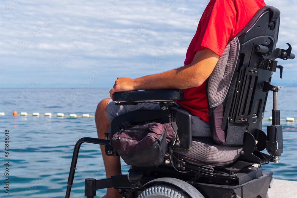 Man sitting in a wheelchair on the beach. Dangers of jumping into water