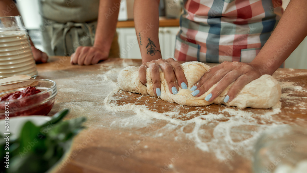 Cropped shot of couple making pizza together. Woman in apron kneading the dough while man helping her in the kitchen. Hobby, lifestyle