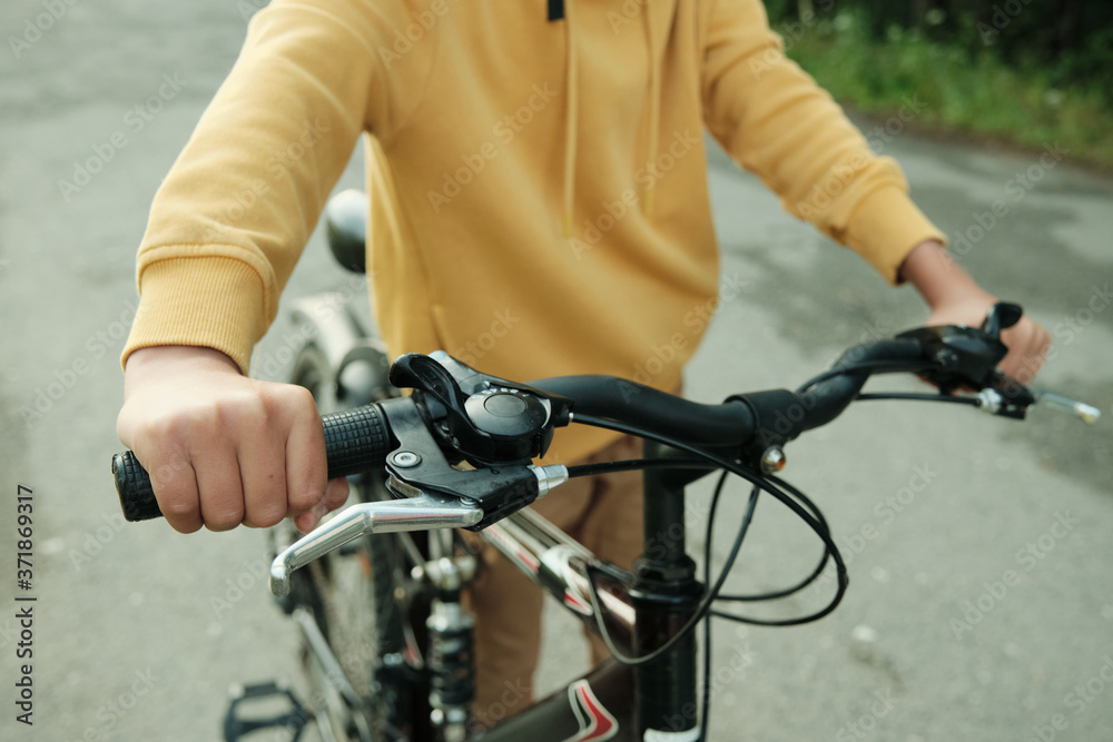 Hand of contemporary teenage boy pushing bicycle while moving down road
