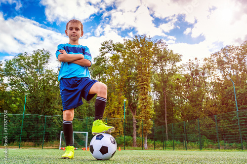 Full length portrait of a kid in sportswear posing with a soccer ball on football field outdoors  © Serhii
