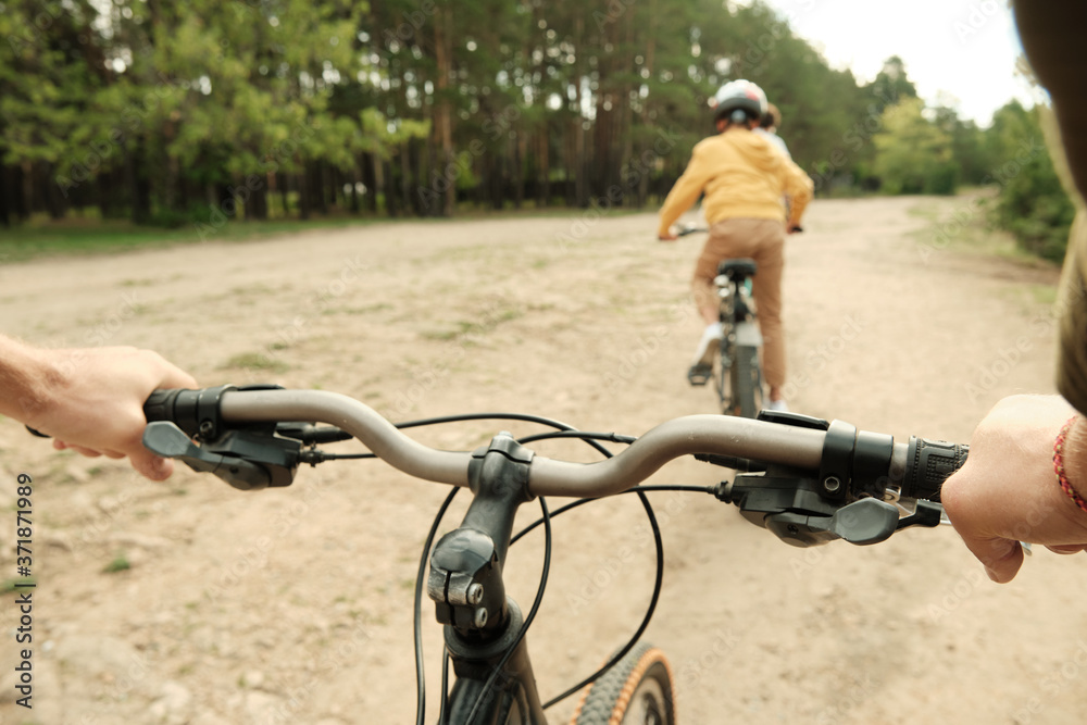 Hands of young man holding by handles of bicycle while following his son Hands of young man holding by handles of bicycle while following his son