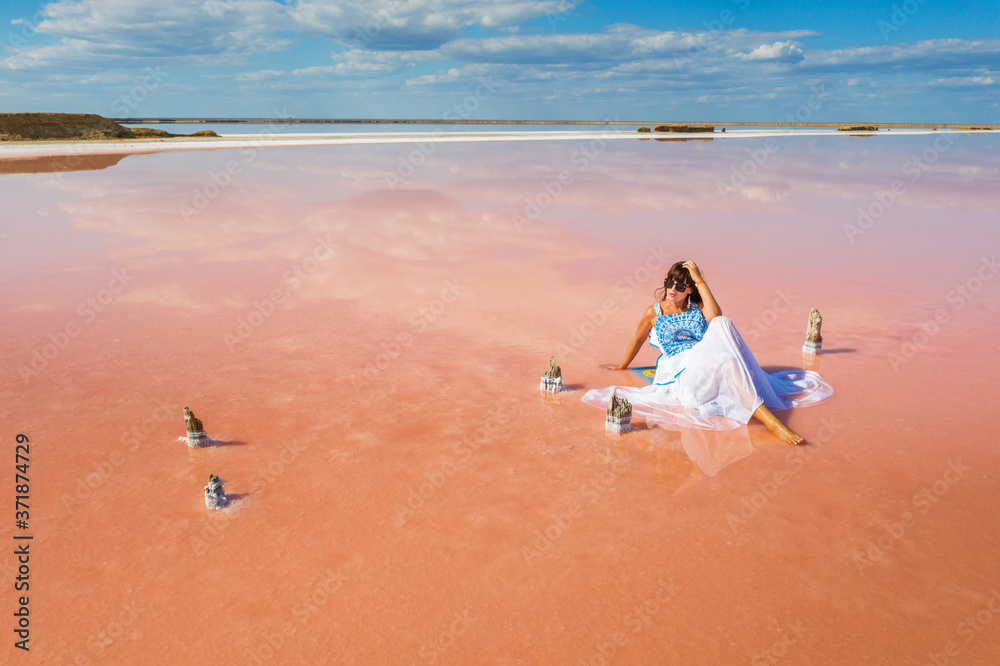 wide angle view to young lady in white dress that seating in pink water of salt lake with copy space