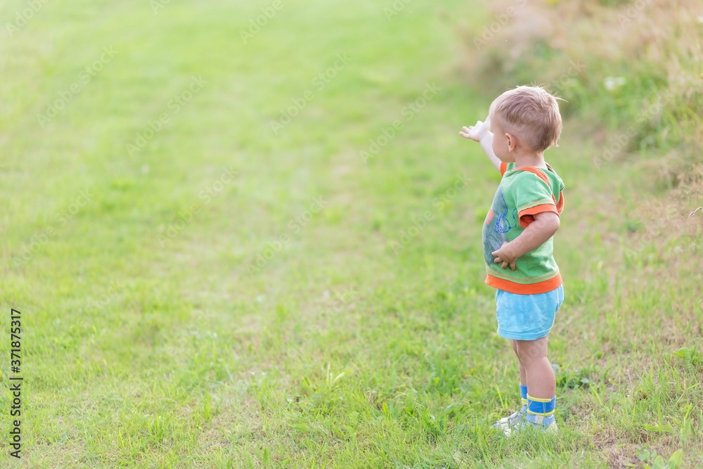 Boy shows his finger the direction while standing on a green lawn Boy shows his finger the direction while standing on a green lawn