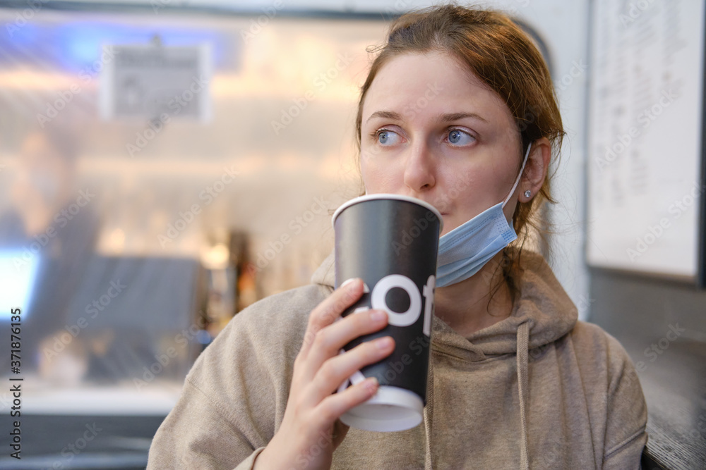 Adult woman in a medical mask drinks coffee in a cafe. Woman in a face mask on a city street, portrait lifestyle Adult woman in a medical mask drinks coffee in a cafe. Woman in a face mask on a city street, portrait lifestyle