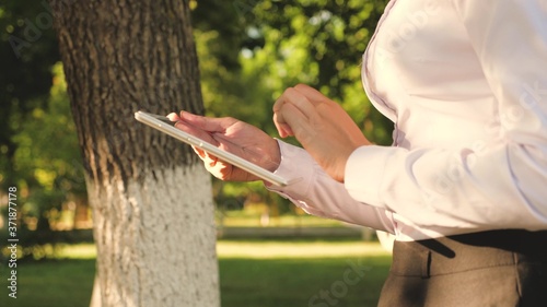 Portrait of a young girl with tablet in her hand. female student teaches lessons on the street with a tablet in the park. Happy woman reading good news in an external message.