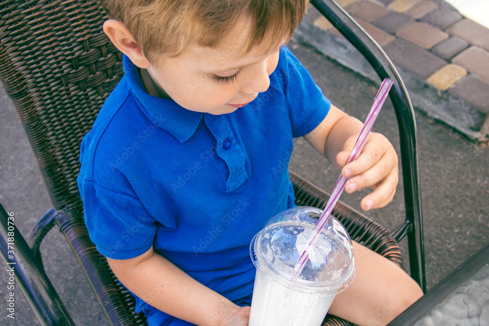 Naklejka premium Little boy drinking milkshake from a plastic cup