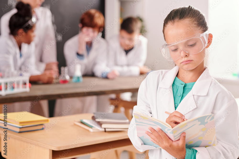 Serious pupil of secondary school in whitecoat and eyeglasses making notes Serious pupil of secondary school in whitecoat and eyeglasses making notes