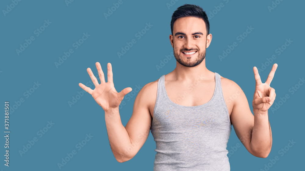 Fototapeta premium Young handsome man wearing swimwear and sleeveless t-shirt showing and pointing up with fingers number seven while smiling confident and happy.