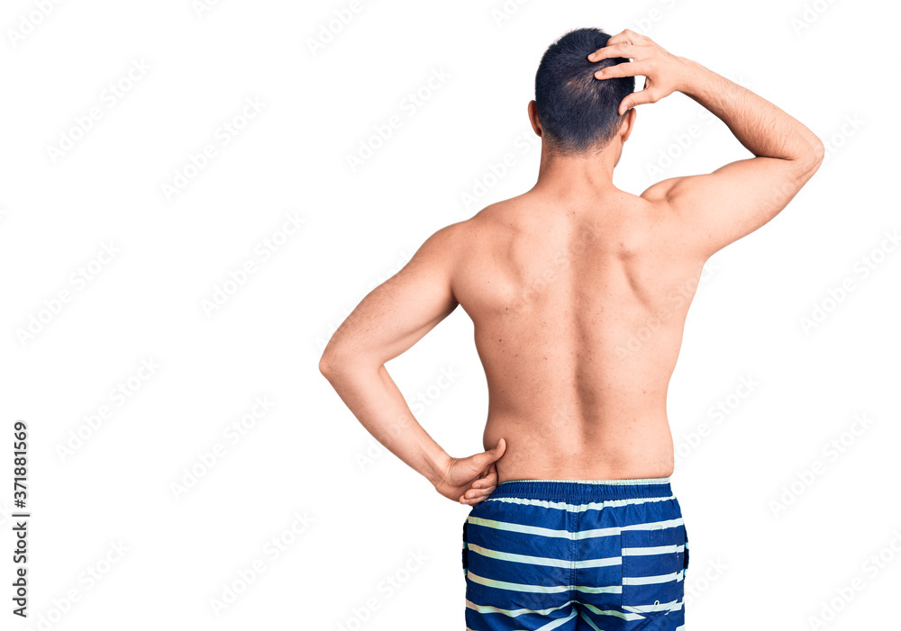 Fototapeta premium Young handsome man wearing swimwear backwards thinking about doubt with hand on head