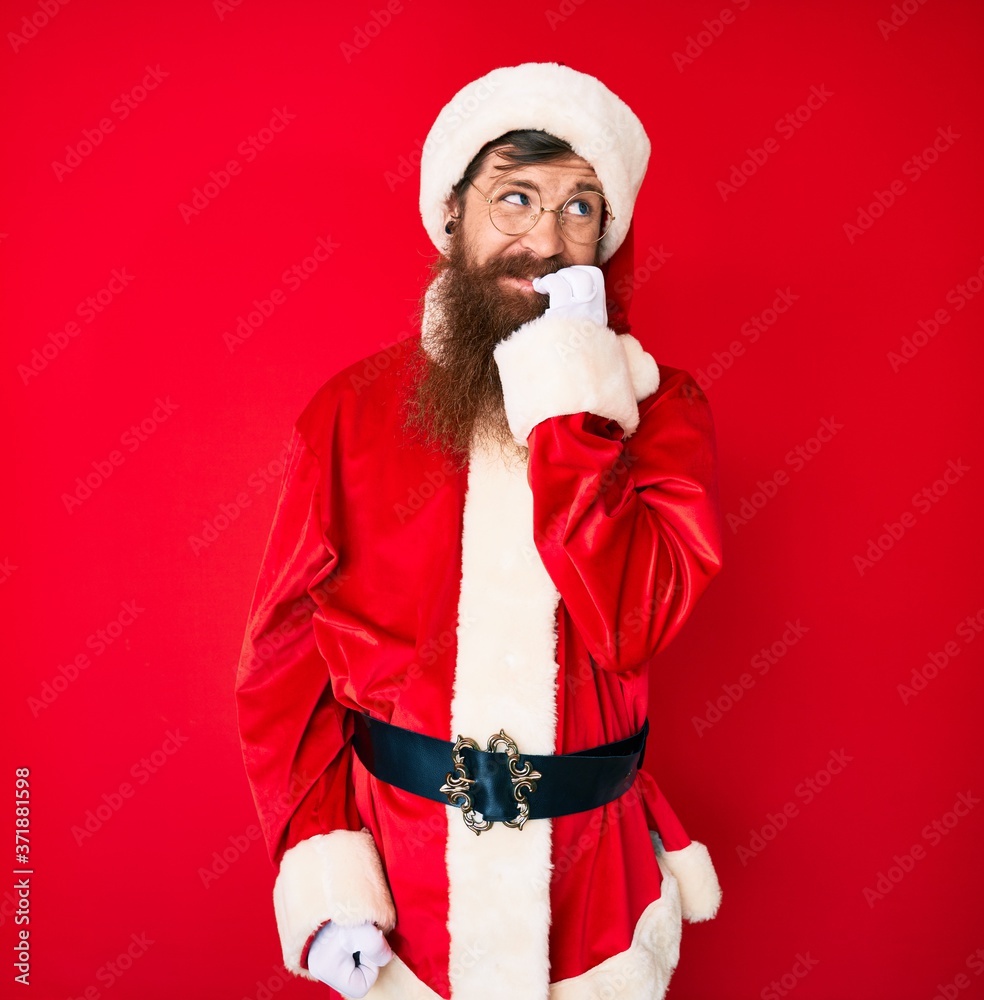 Handsome young red head man with long beard wearing santa claus costume looking stressed and nervous with hands on mouth biting nails. anxiety problem. Handsome young red head man with long beard wearing santa claus costume looking stressed and nervous with hands on mouth biting nails. anxiety problem.