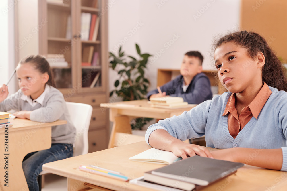 Serious mixed-race student and her classmates looking at teacher attentively