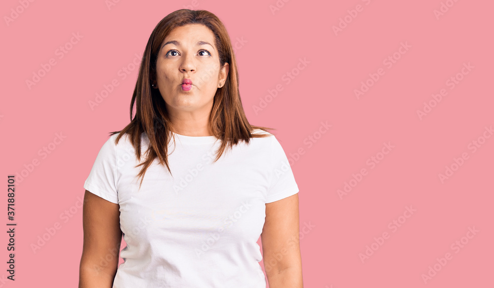 Middle age latin woman wearing casual white tshirt making fish face with lips, crazy and comical gesture. funny expression. Middle age latin woman wearing casual white tshirt making fish face with lips, crazy and comical gesture. funny expression.