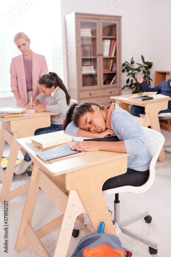 Mixed-race tired or bored schoolgirl in casualwear napping on desk at lesson