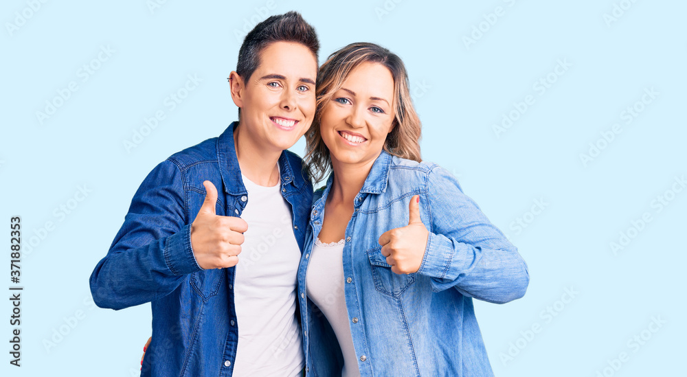 Couple of women wearing casual clothes success sign doing positive gesture with hand, thumbs up smiling and happy. cheerful expression and winner gesture.