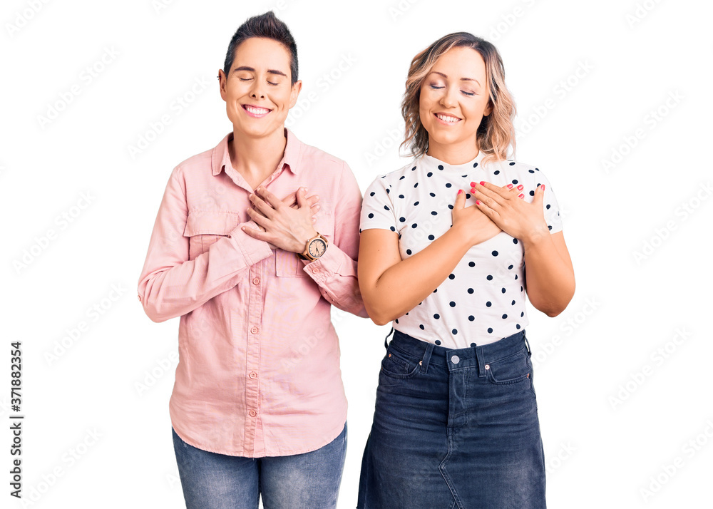 Couple of women wearing casual clothes smiling with hands on chest with closed eyes and grateful gesture on face. health concept. Couple of women wearing casual clothes smiling with hands on chest with closed eyes and grateful gesture on face. health concept.