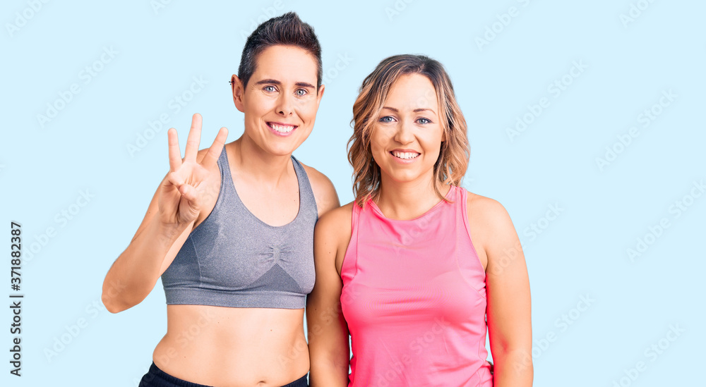 Couple of women wearing sportswear showing and pointing up with fingers number three while smiling confident and happy. Couple of women wearing sportswear showing and pointing up with fingers number three while smiling confident and happy.