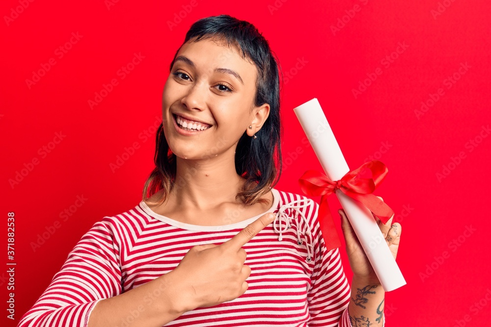 Young woman holding graduate degree diploma smiling happy pointing with hand and finger Young woman holding graduate degree diploma smiling happy pointing with hand and finger