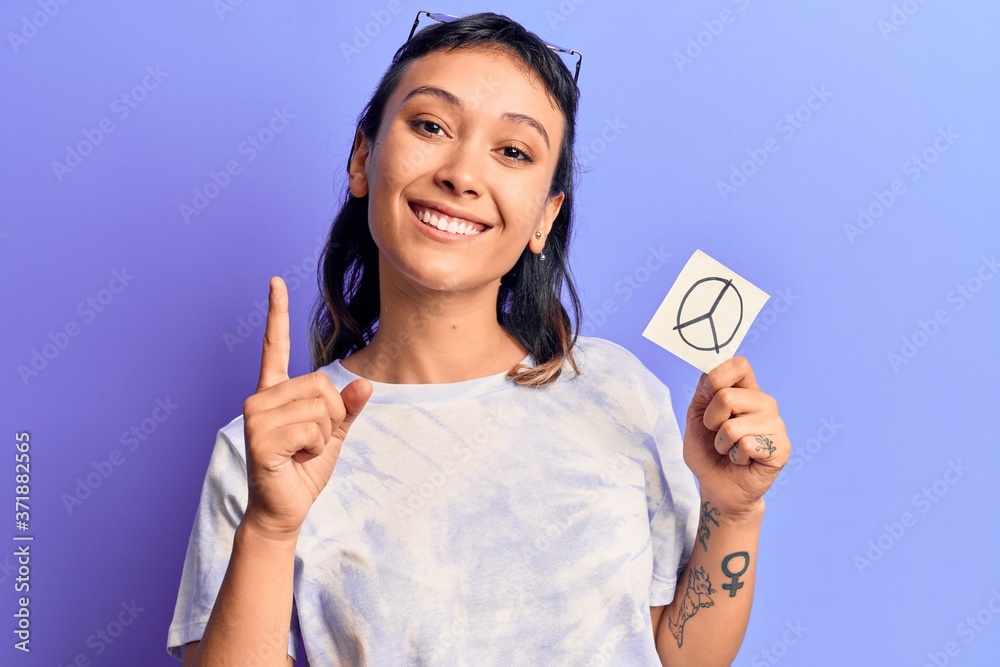 Young woman holding peace symbol reminder paper smiling with an idea or question pointing finger with happy face, number one Young woman holding peace symbol reminder paper smiling with an idea or question pointing finger with happy face, number one