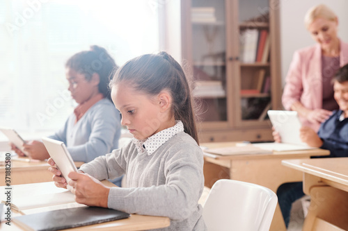 Serious clever girl and her classmates with tablets working individually