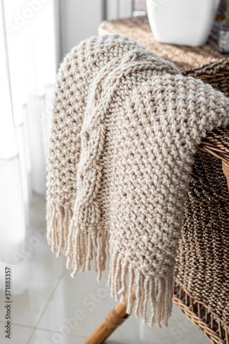 Detail of hand-woven beige wool blanket on wicker chair.