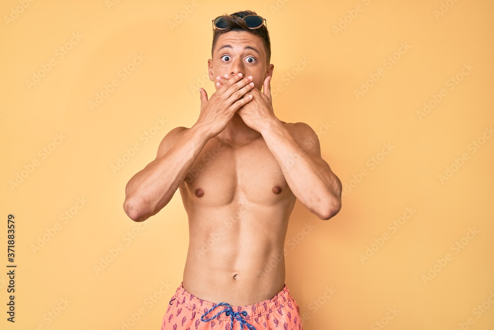 Young hispanic boy wearing swimwear shirtless shocked covering mouth with hands for mistake. secret concept.