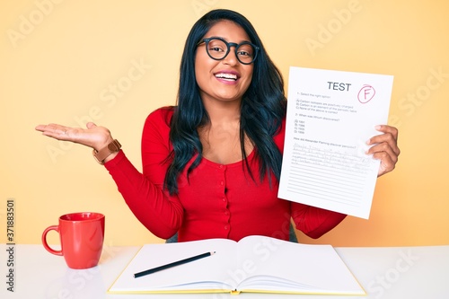 Beautiful latin young woman with long hair showing a failed exam celebrating victory with happy smile and winner expression with raised hands