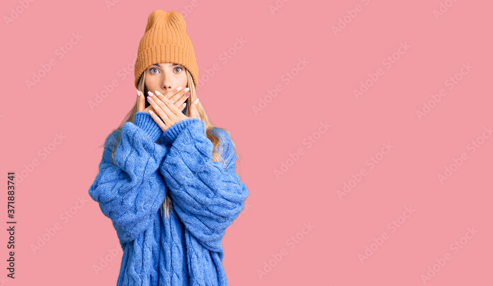 Beautiful caucasian woman with blonde hair wearing wool sweater and winter hat shocked covering mouth with hands for mistake. secret concept.