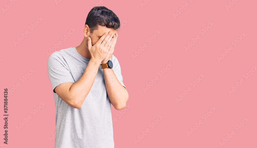 Handsome young man with bear wearing casual tshirt with sad expression covering face with hands while crying. depression concept. Handsome young man with bear wearing casual tshirt with sad expression covering face with hands while crying. depression concept.