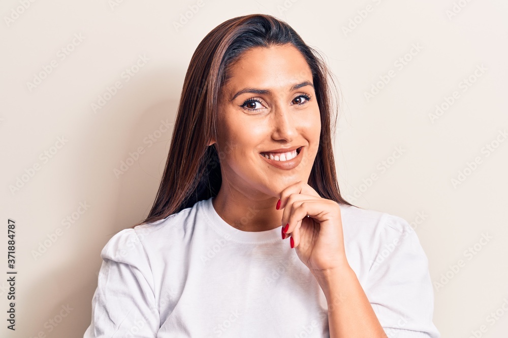 Young beautiful brunette woman wearing casual t-shirt smiling looking confident at the camera with crossed arms and hand on chin. thinking positive. Young beautiful brunette woman wearing casual t-shirt smiling looking confident at the camera with crossed arms and hand on chin. thinking positive.