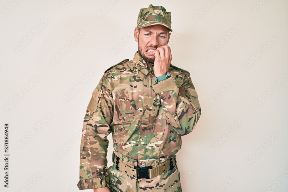 Young caucasian man wearing camouflage army uniform looking stressed and nervous with hands on mouth biting nails. anxiety problem. Young caucasian man wearing camouflage army uniform looking stressed and nervous with hands on mouth biting nails. anxiety problem.
