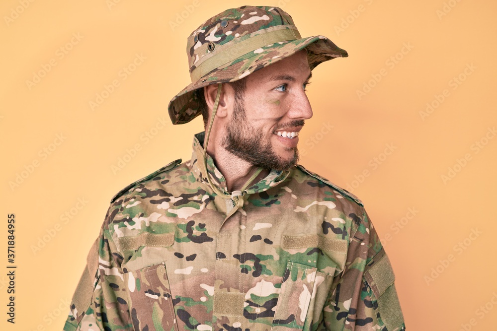Young caucasian man wearing camouflage army uniform looking to side, relax profile pose with natural face and confident smile.