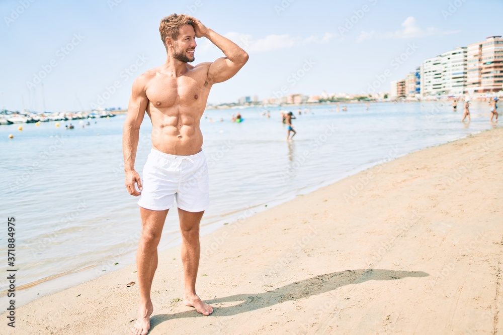 Handsome fitness caucasian man at the beach on a sunny day showing muscular fitness body