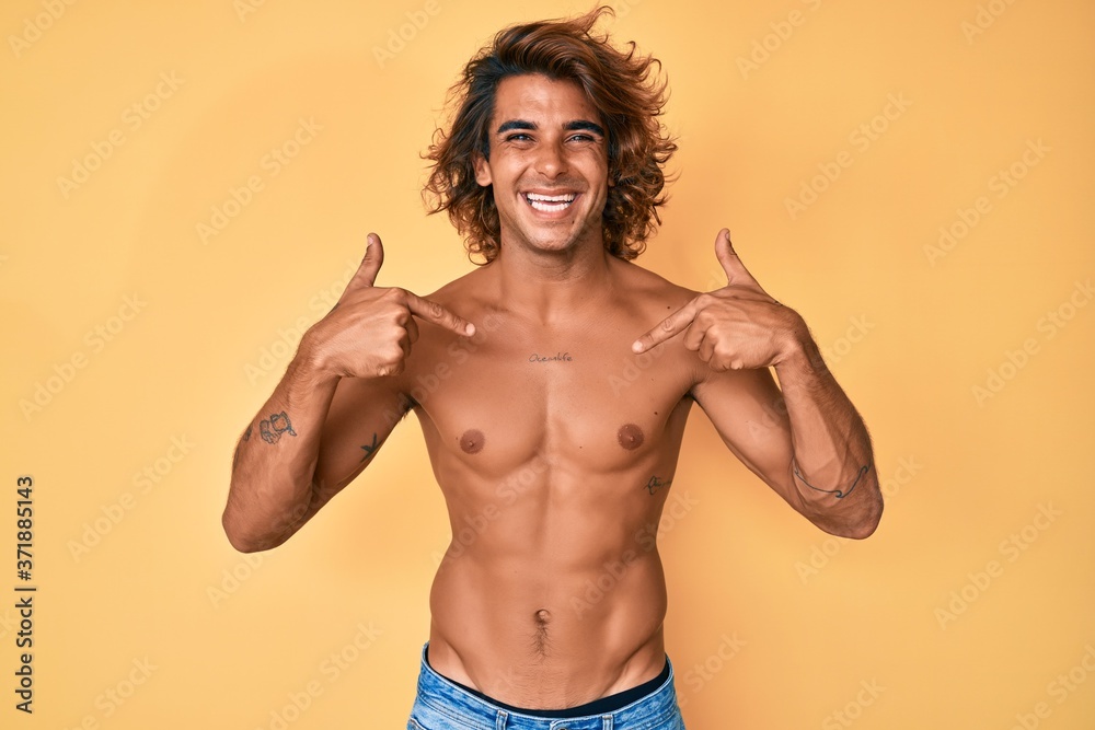 Young hispanic man standing shirtless looking confident with smile on face, pointing oneself with fingers proud and happy.