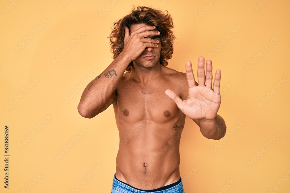 Fototapeta premium Young hispanic man standing shirtless covering eyes with hands and doing stop gesture with sad and fear expression. embarrassed and negative concept.