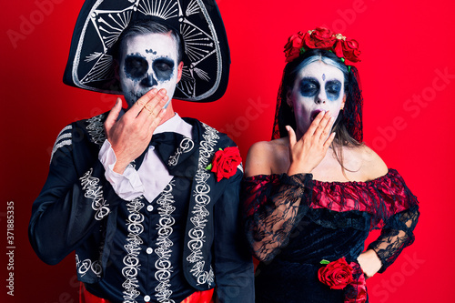 Young couple wearing mexican day of the dead costume over red bored yawning tired covering mouth with hand. restless and sleepiness.