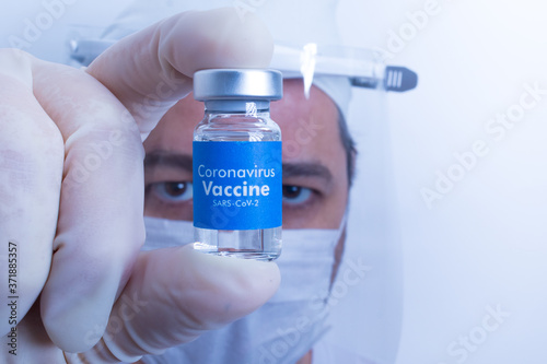 Médico com luva cirúrgica segurando um frasco de vacina com o rótulo azul escrito Vacina Coronavírus - Sars-Cov-2 sobre o fundo branco photo