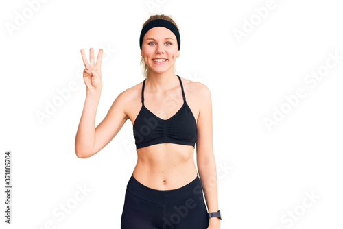 Young beautiful blonde woman wearing sportswear showing and pointing up with fingers number three while smiling confident and happy. © Krakenimages.com