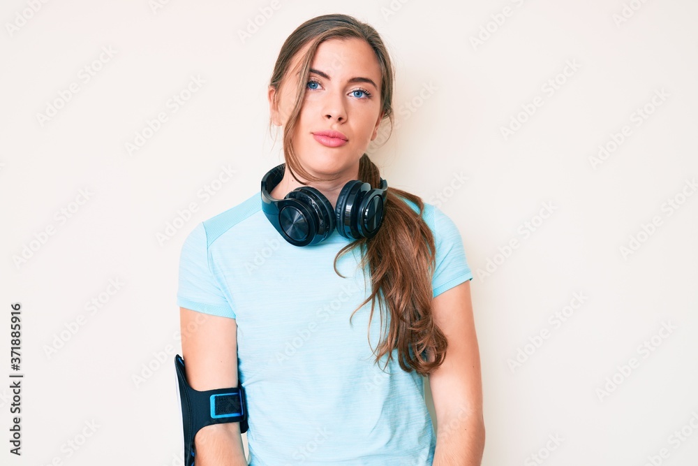 Beautiful young caucasian woman wearing gym clothes and using headphones relaxed with serious expression on face. simple and natural looking at the camera. Beautiful young caucasian woman wearing gym clothes and using headphones relaxed with serious expression on face. simple and natural looking at the camera.