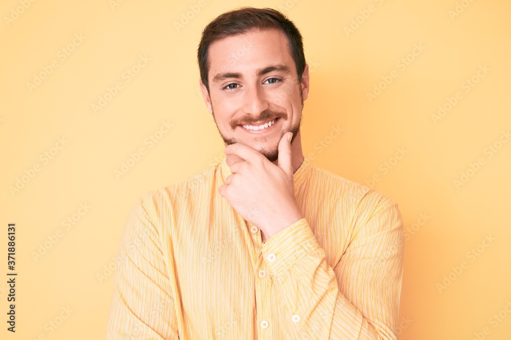 Young handsome man wearing casual clothes looking confident at the camera smiling with crossed arms and hand raised on chin. thinking positive. Young handsome man wearing casual clothes looking confident at the camera smiling with crossed arms and hand raised on chin. thinking positive.