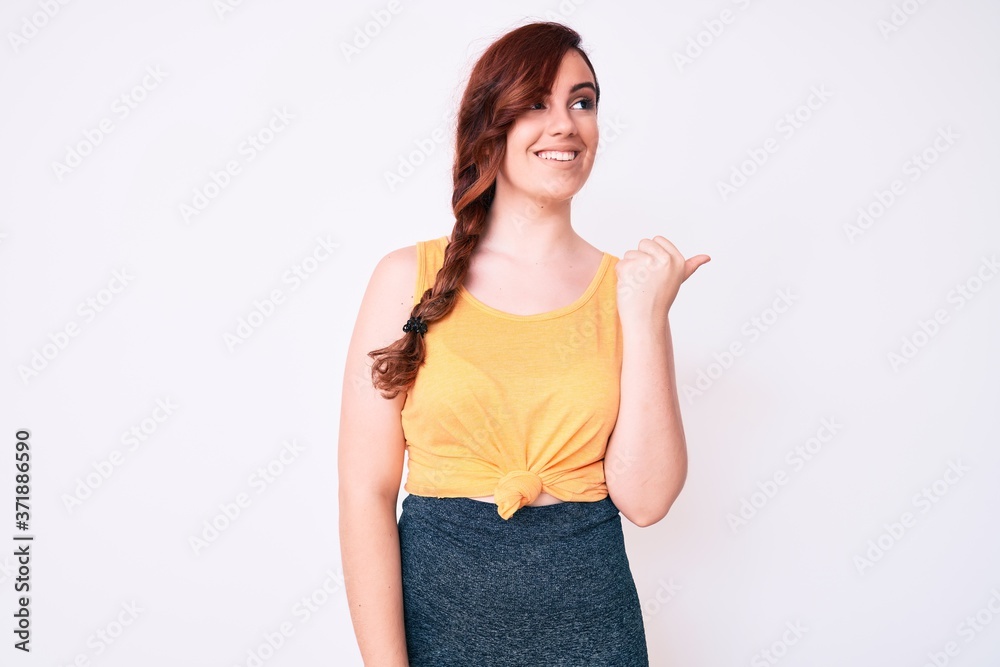 Young beautiful woman wearing casual clothes pointing thumb up to the side smiling happy with open mouth