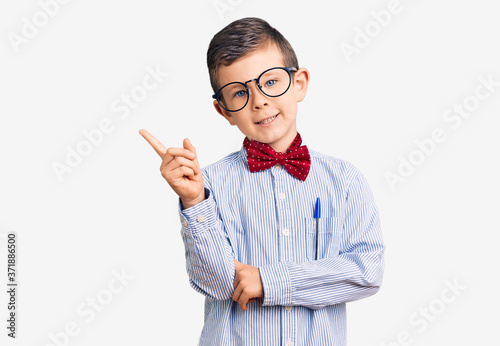 Cute blond kid wearing nerd bow tie and glasses smiling happy pointing with hand and finger to the side