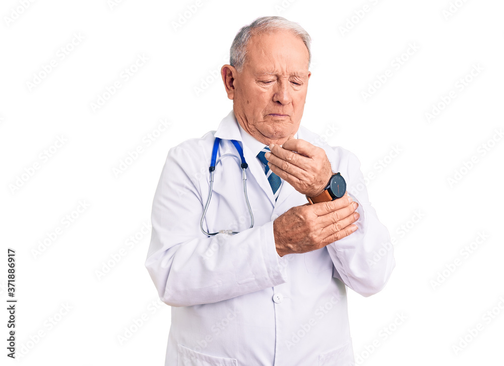 Senior handsome grey-haired man wearing doctor coat and stethoscope suffering pain on hands and fingers, arthritis inflammation Senior handsome grey-haired man wearing doctor coat and stethoscope suffering pain on hands and fingers, arthritis inflammation